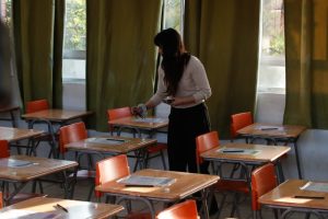 Mujer en aula con escritorios vacíos.