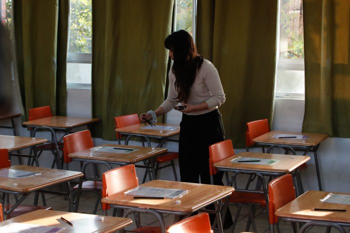 Mujer en aula con escritorios vacíos.