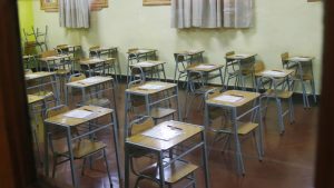 Aula vacía con escritorios desordenados.