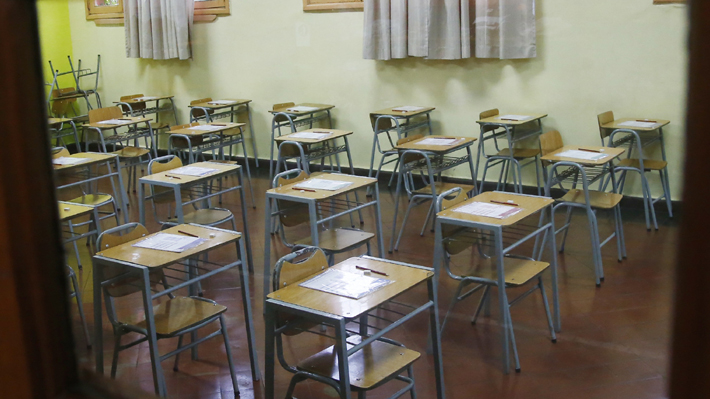 Aula vacía con escritorios desordenados.